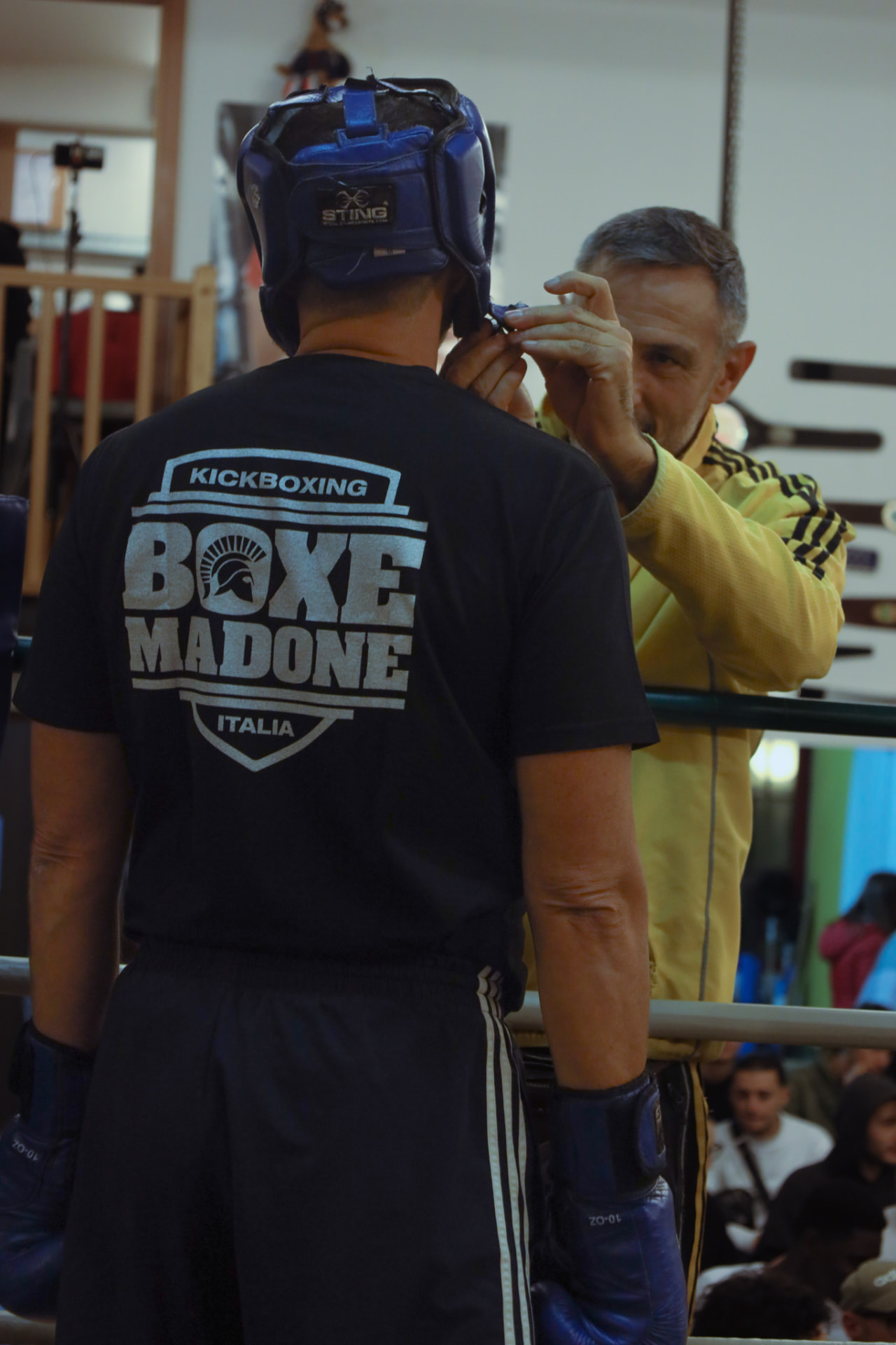 Coach adjusting a fighter's headgear at Boxe Madone Italia
