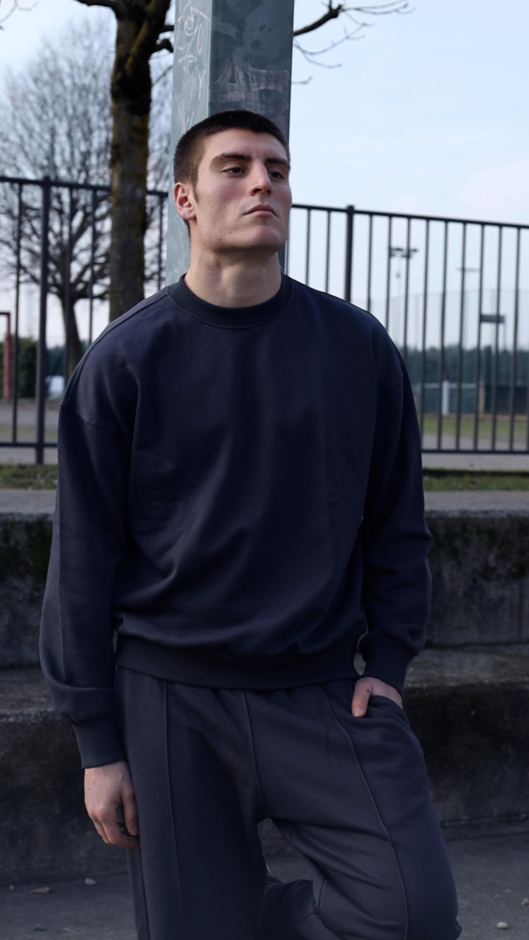 Streetwear portrait in navy sweatsuit by a park fence