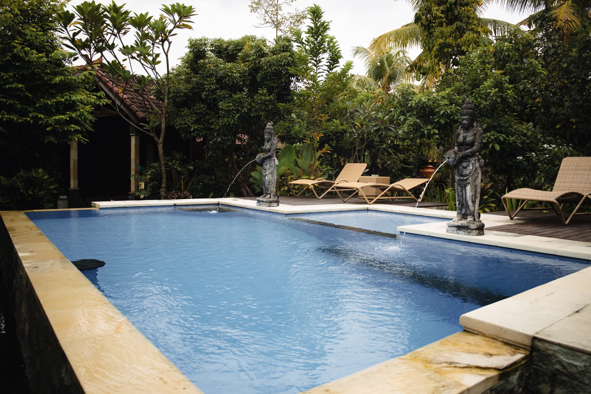Villa pool with stone statue fountains and sun loungers in Bali