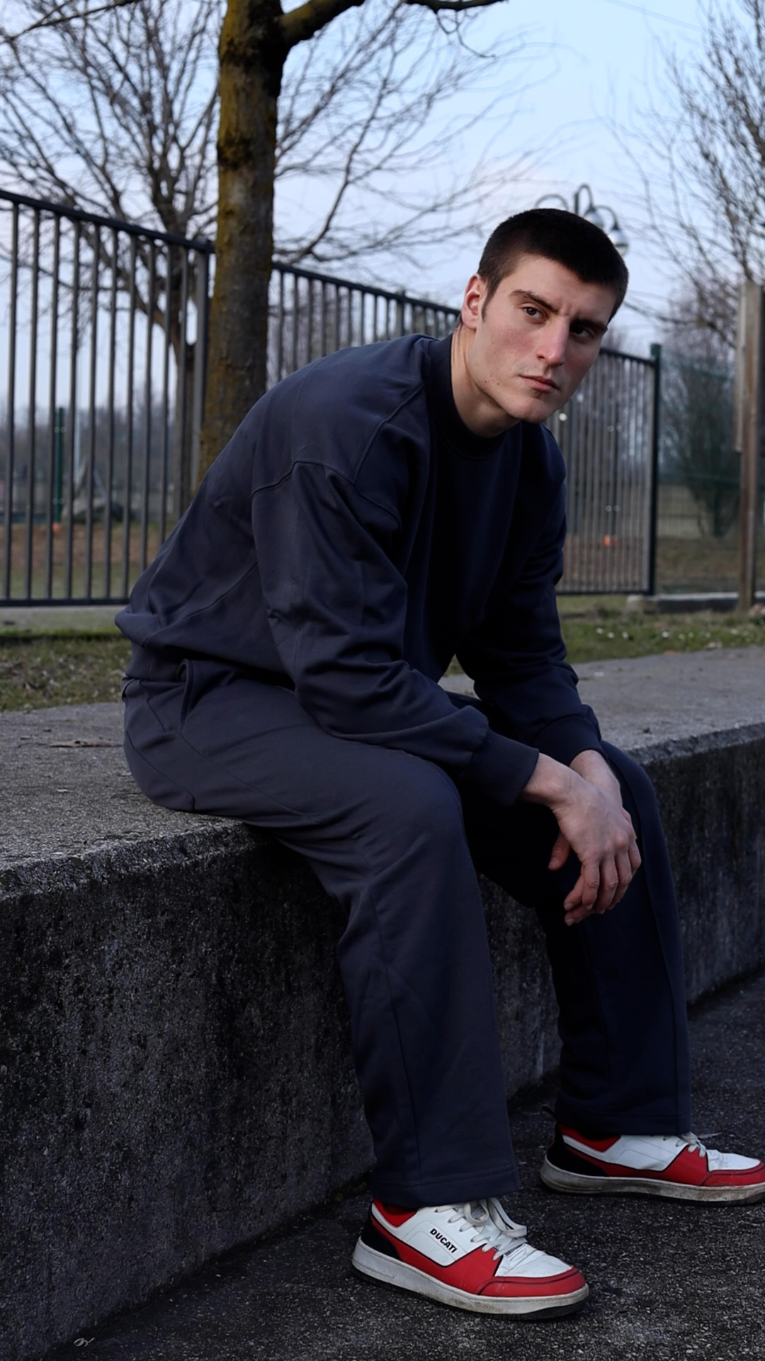 Seated streetwear portrait on a concrete ledge at dusk